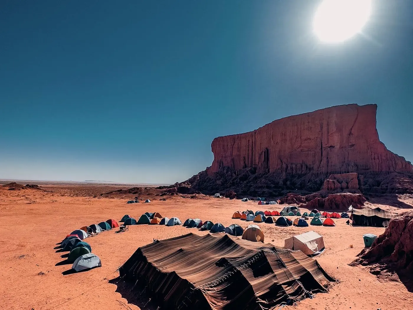 A camp of nomad tents beneath a flat-topped red gara near El Bayadh