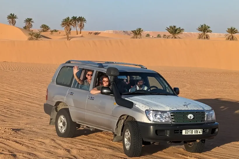 Travellers waving from a Land Cruiser crossing the dunes near El Menia