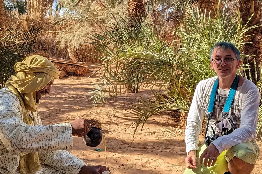 A host preparing tea for a traveller in a palm grove at Timimoun