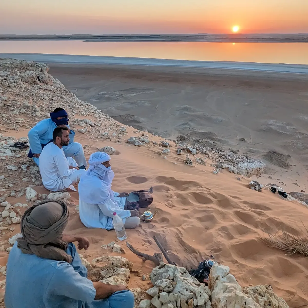 The group sitting on a rocky ridge as the sun sets over the sebkha at El Menia