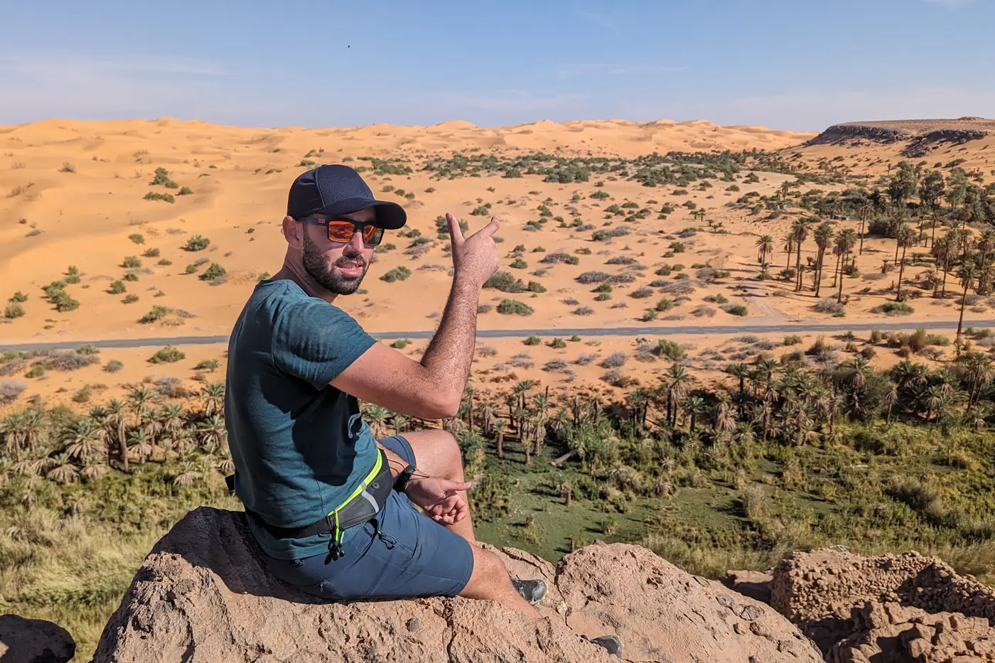A traveller sitting on a rock above the palm groves and dunes of Taghit