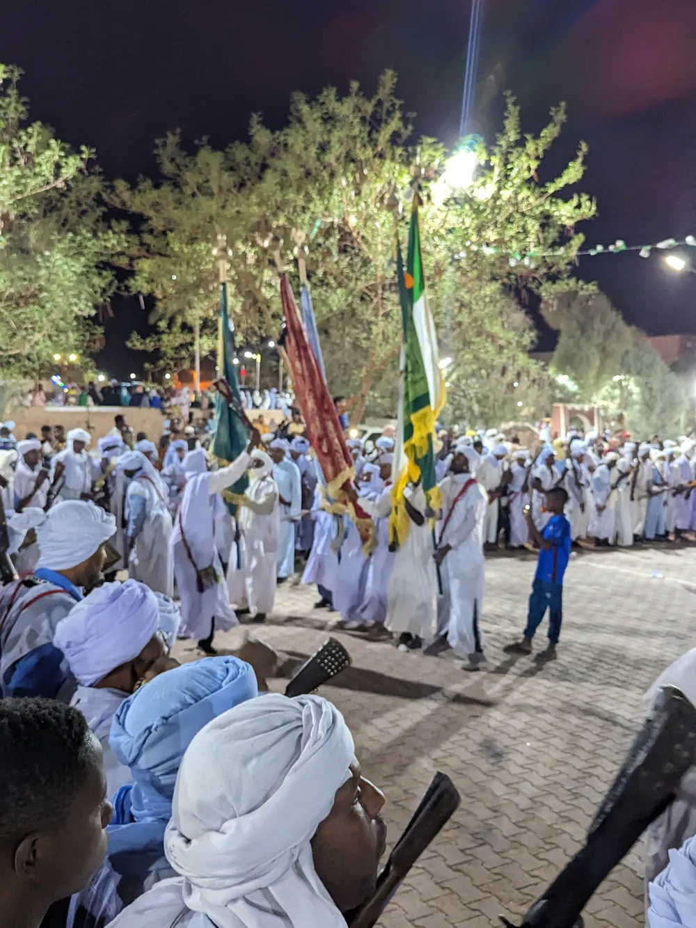 A crowd in white robes at a night festival in Timimoun